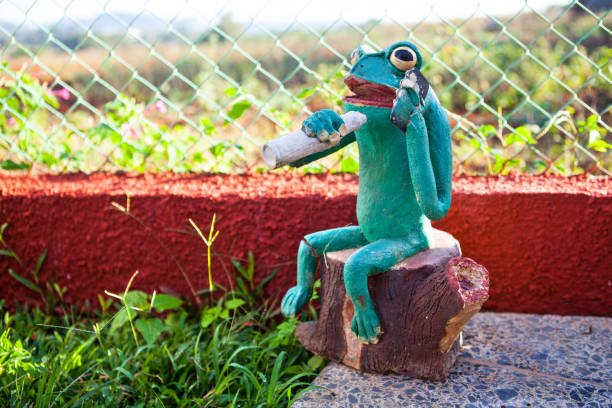 Green frog figurine sitting on wooden stump holding joint and talking on phone blog photo